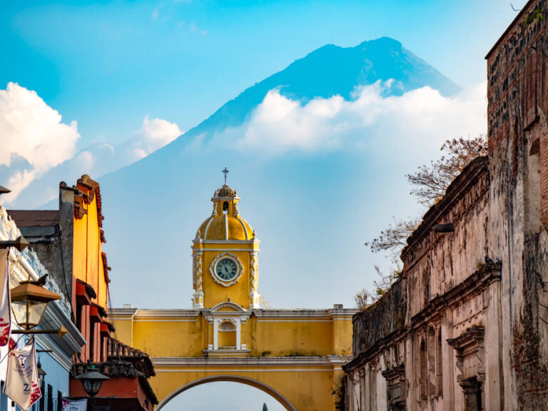 The yellow Arco de Santa Catalina standing in front of the looming Volcán de Agua in Antigua, Guatemala.
