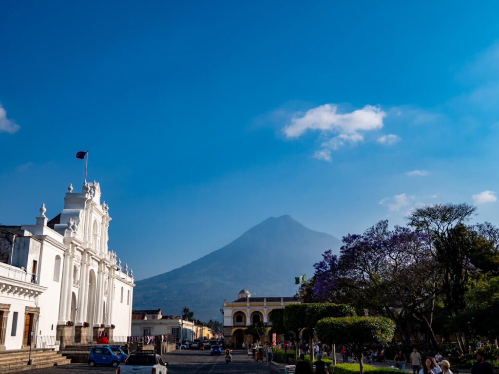 The white façade of the San Jose Cathedral standing on the edge of Parque Central in Antigua Guatemala, with a clear view of Agua Volcano.