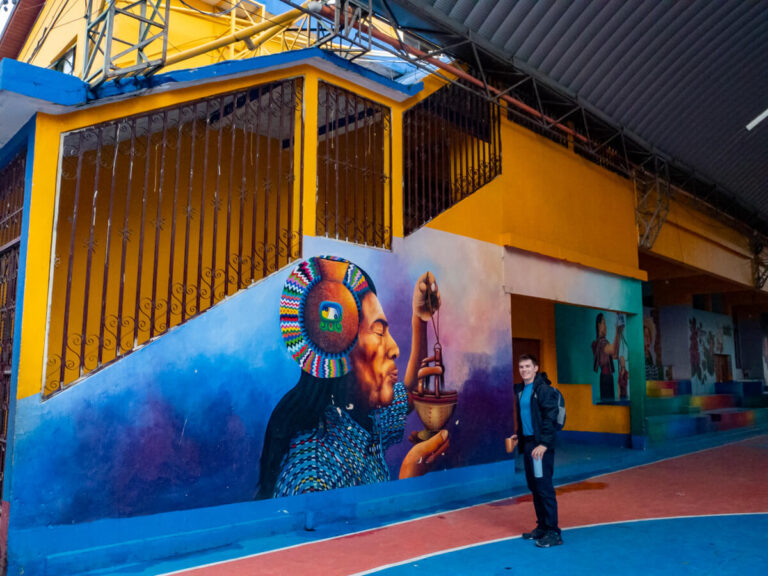Dan standing by a colourful mural of an indigenous Maya man in Lake Atitlán, Guatemala.