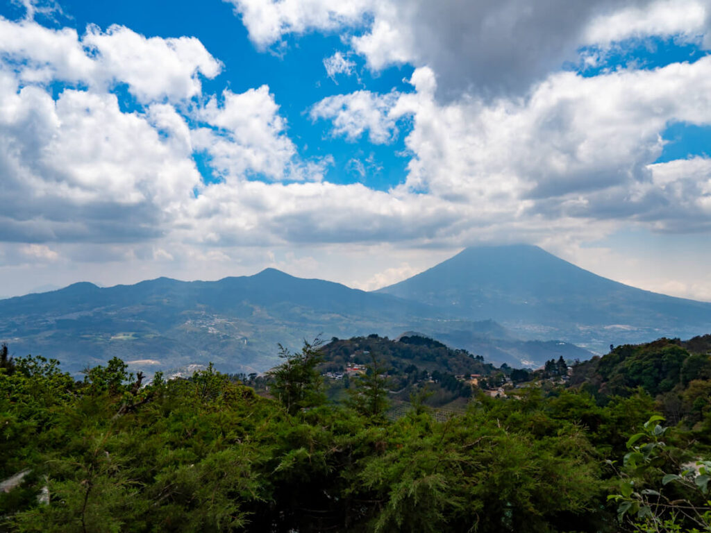 Rolling hills leading to a cloudy view of Agua Volcano in the highlands near Antigua, Guatemala.
