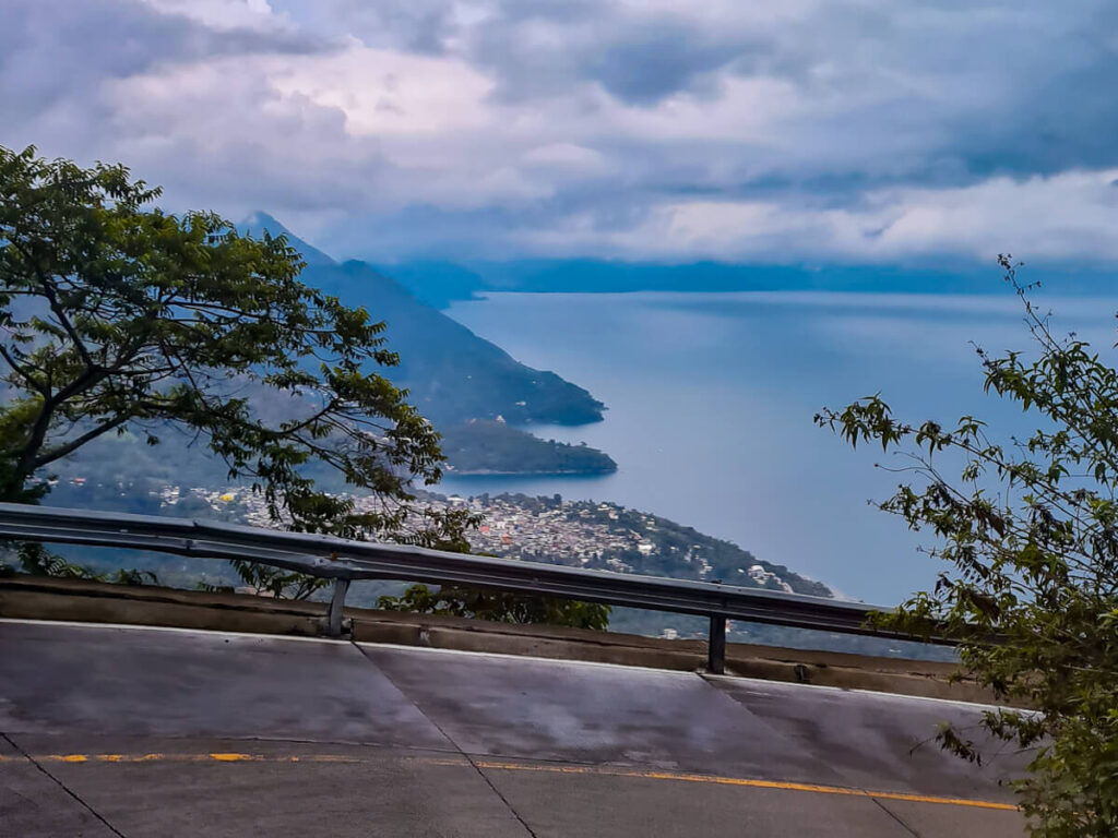 A steep, winding mountain road with a view of towns on the shore of Lake Atitlán, Guatemala.
