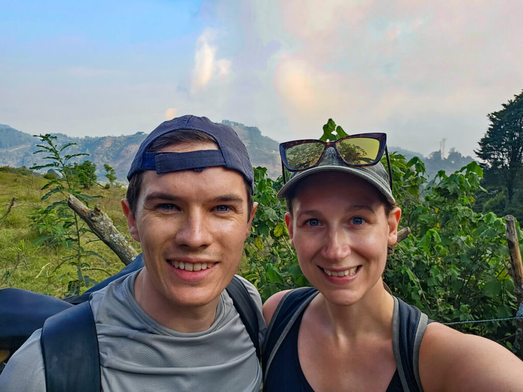 Dan and Lucy smiling at the camera in front of lush forest on a hiking trail on Pacaya Volcano.