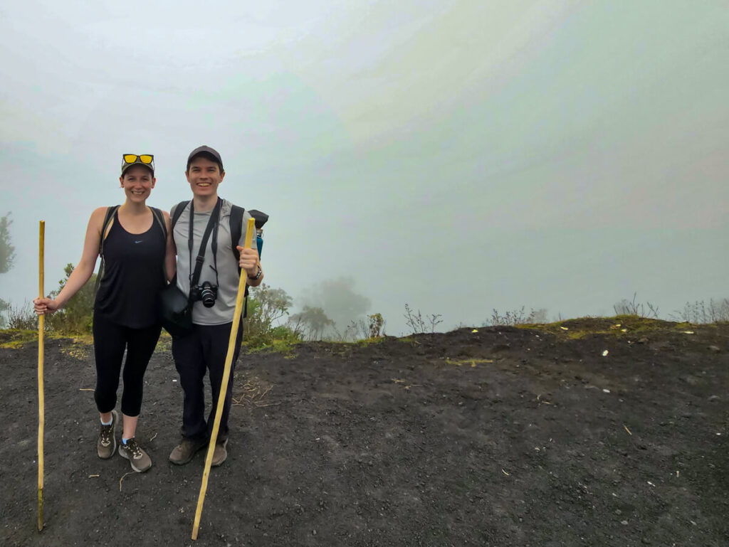 Lucy and Dan holding sticks in front of thick cloud on Pacaya Volcano.