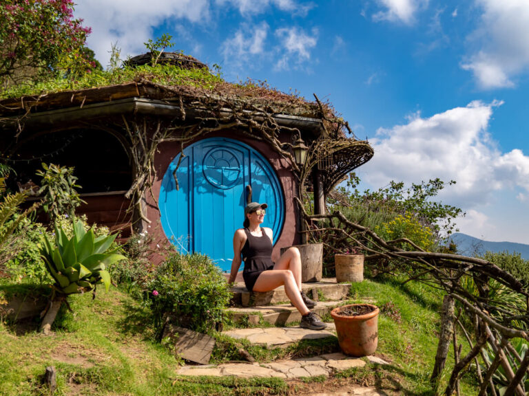 Lucy looking away while sitting on steps leading to a hobbit house with a blue door in Hobbitenango, Antigua.