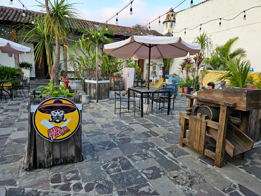 A sign for Mr Taco, one of the best places to eat in Antigua, Guatemala, in a courtyard filled with tables and plants.