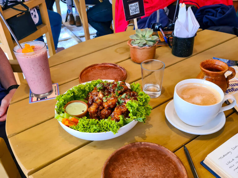 A plate of cauliflower wings, a pink smoothie, and a cup of coffee on a table in Once Once, one of the best places to eat in Antigua, Guatemala.
