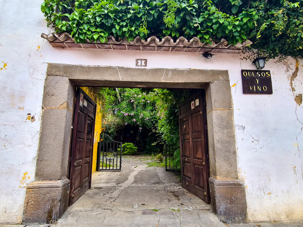A stone doorway leading to a leafy courtyard of Quesos y Vino in Antigua, Guatemala.