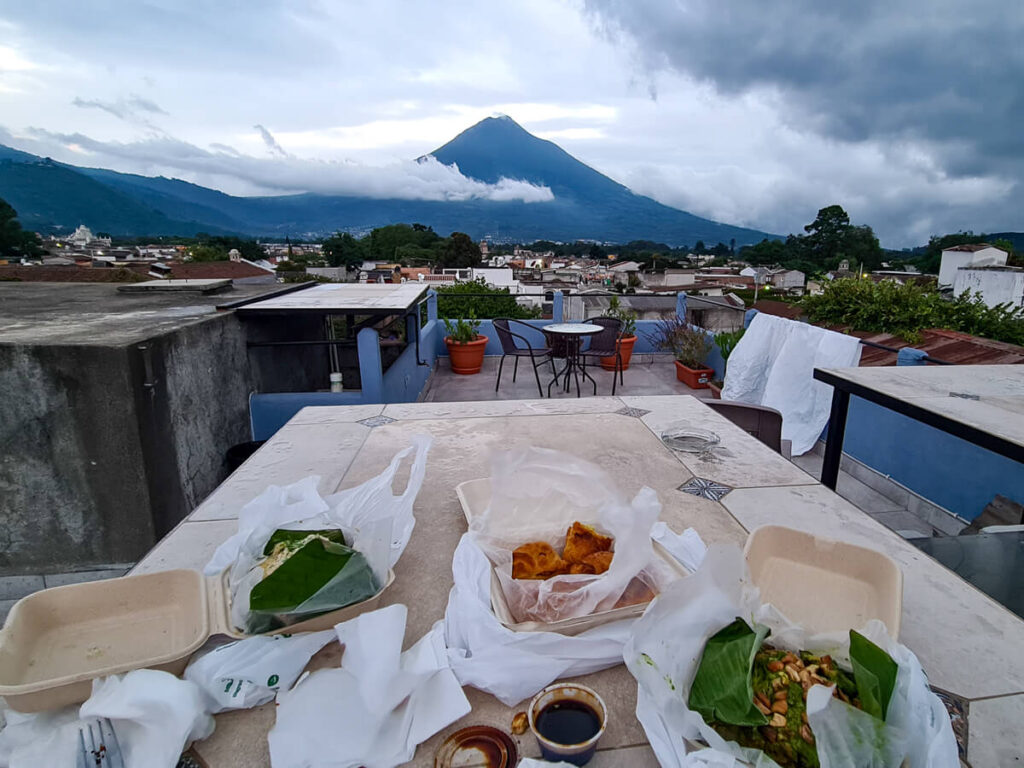 Takeaway containers lined with banana leaves on a table on a rooftop terrace with views of Agua Volcano in Antigua, Guatemala.