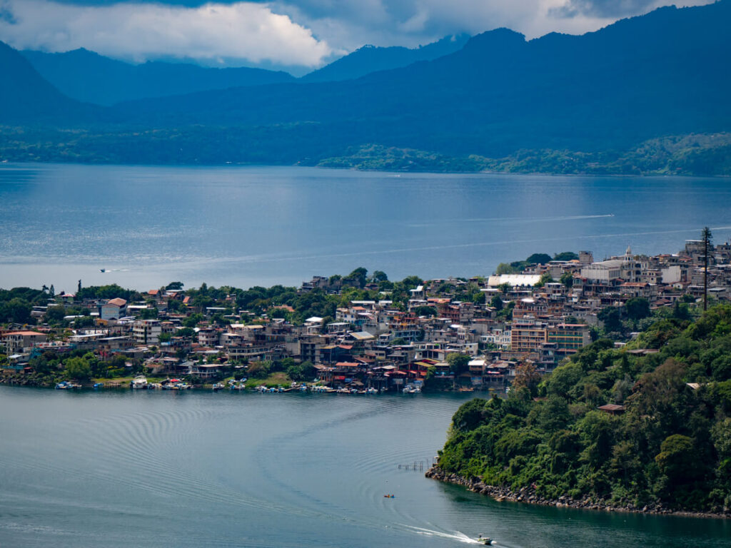 A lancha leaving the hilly town of San Pedro La Laguna, surrounded by green mountains on the shore of Lake Atitlán