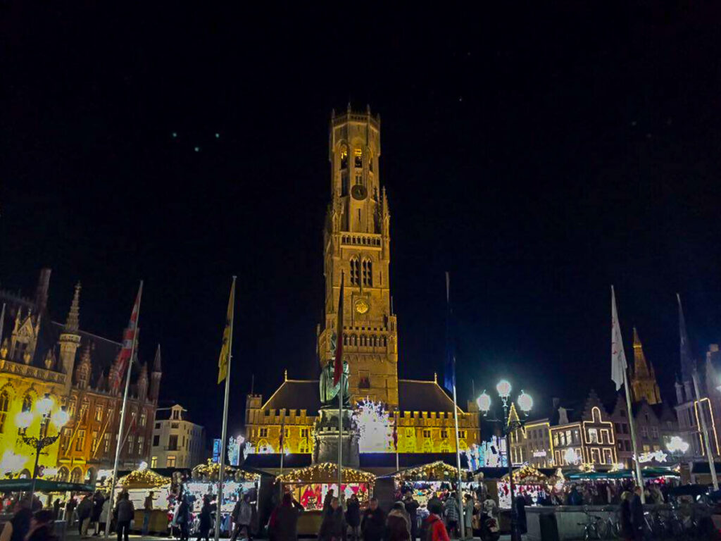Christmas Market stalls covered in fairy lights in front of the famous clock tower in Bruges.