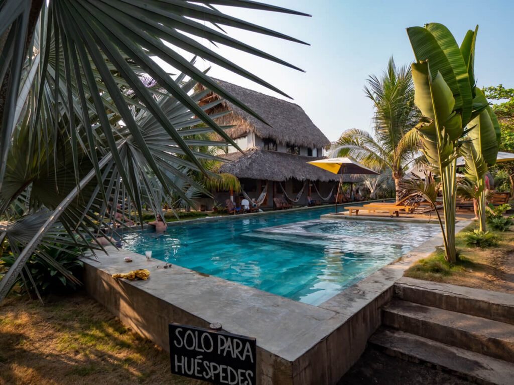 A large pool surrounded by palm trees and hammocks in the courtyard in Cocori Lodge, a beachfront hotel in El Paredón, Guatemala.