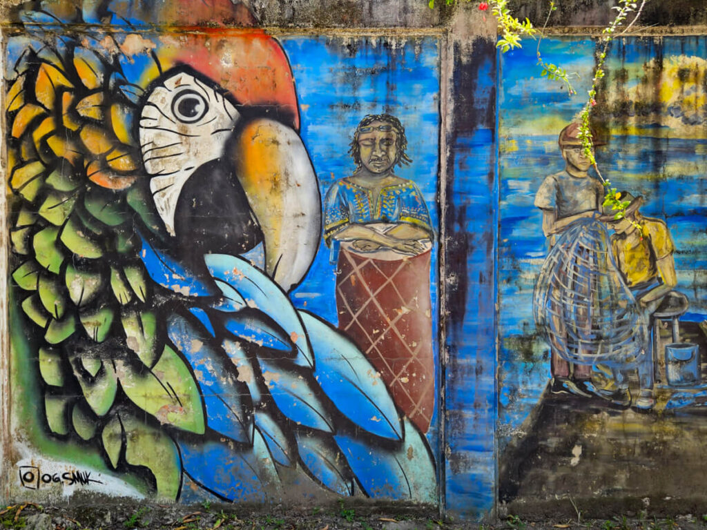 A colourful mural of a parrot and Garifuna people playing drums on a wall in Livingston.