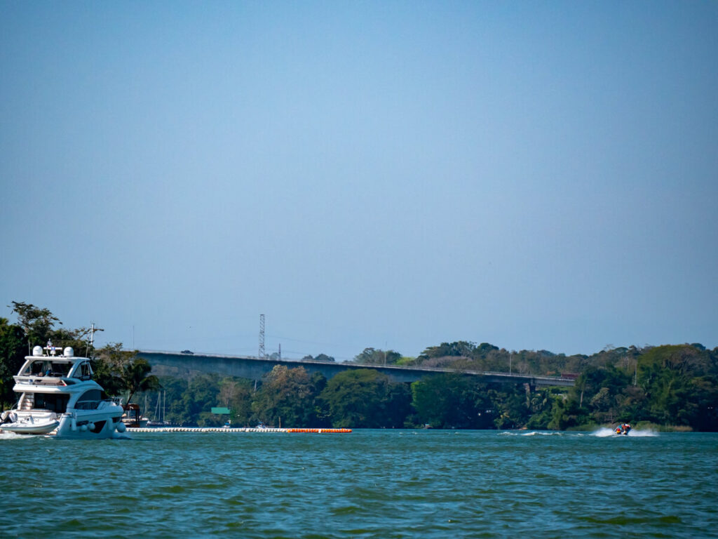A yacht driving towards a large bridge crossing the Río Dulce in Guatemala.