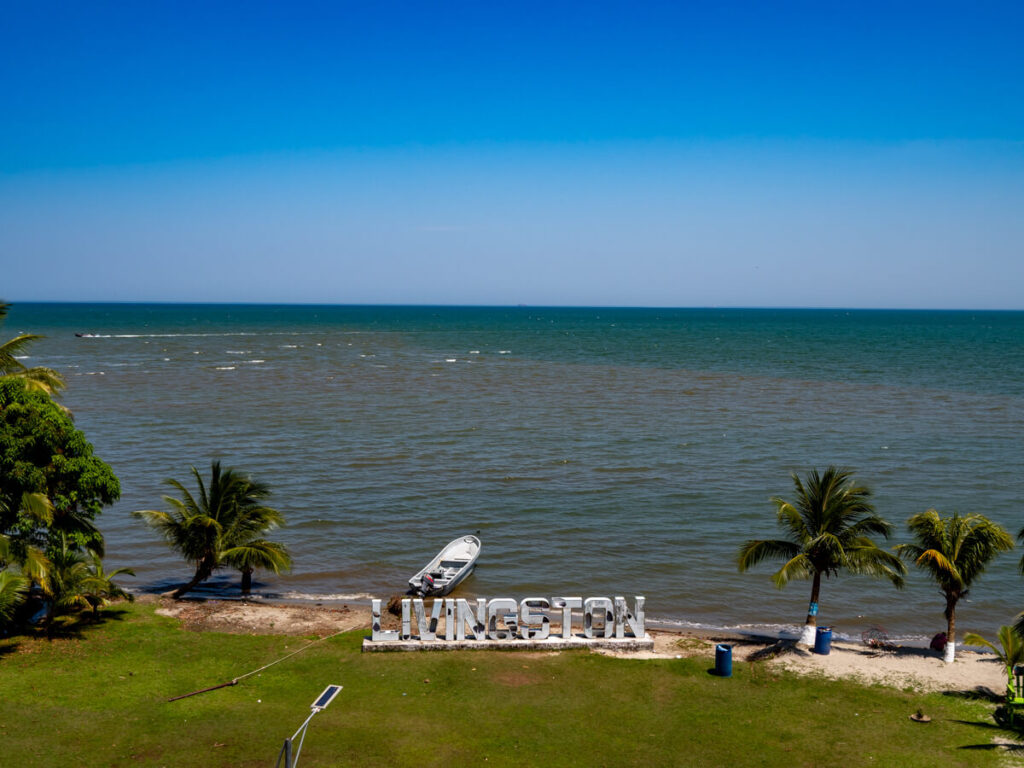 A beach backed by the Caribbean Sea with a sign spelling Livingston.
