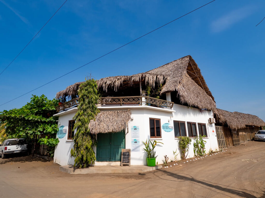 The white façade and thatched palapa roof of a restaurant in El Paredón, Guatemala.