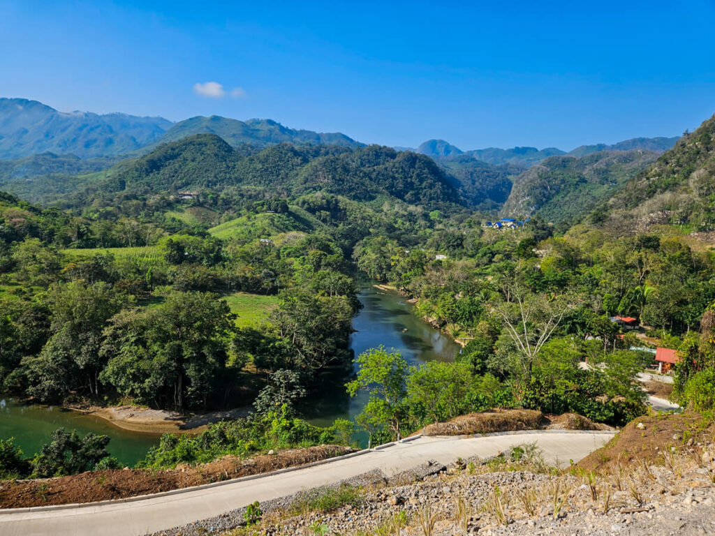 A road overlooking a river winding through a mountainous valley on the route between Lanquín and Semuc Champey.