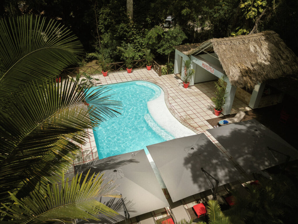 A thatched roof building and outdoor pool in Hostal Jungle Lodge Tikal.