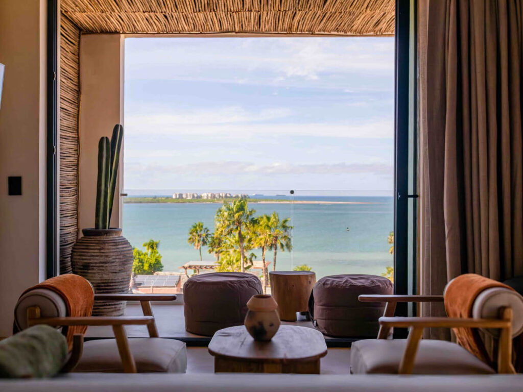 Lounge chairs in front of a wide window overlooking the sea in a hotel room in Republica Pagana, one of the best hotels in La Paz, Mexico.