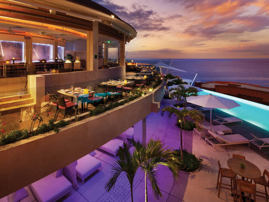 An infinity pool overlooking the sea with a bar lit up at night in The Westin Los Cabos Resort Villas.