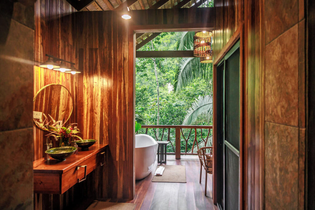 A wooden hotel room leading to a bath and balcony overlooking the jungle in Sweet Songs Jungle Lodge in Belize.