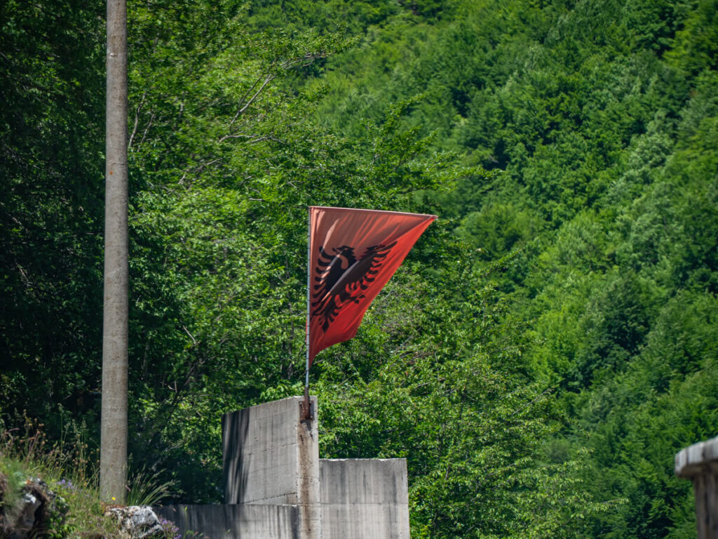 The flag of Albania flying against a lush green mountain.