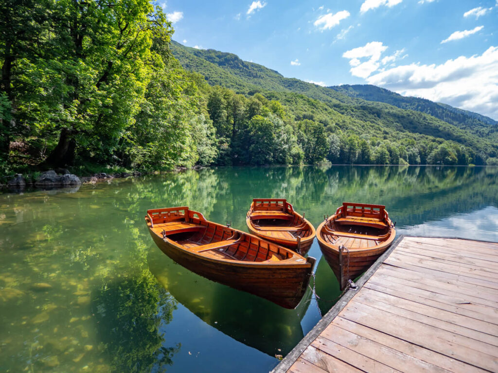 Three wooden rowboats moored to a dock on the edge of a lake in Biogradska Gora National Park.