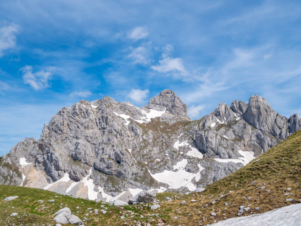 A grassy ridgeline under the limestone mountain range that contains the peak of Bobotov Kuk.