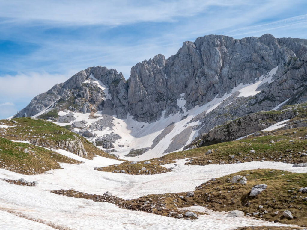 Snow laying across grey limestone mountains and a green valley on the Bobotov Kuk trail.