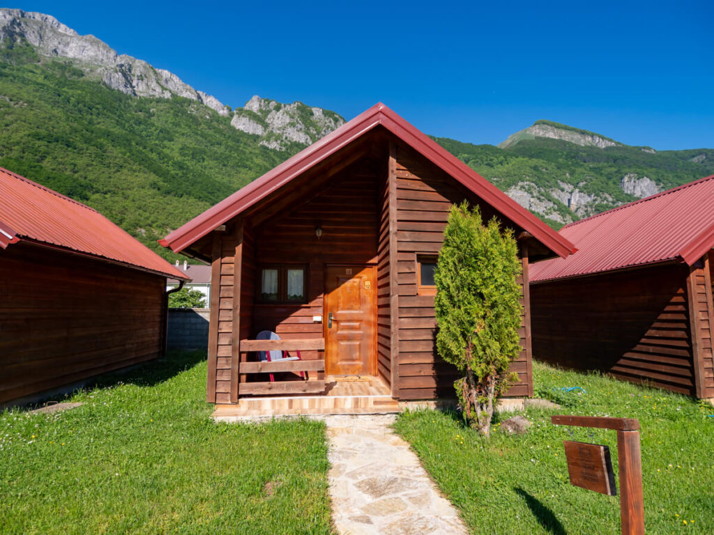 A wooden cabin with a red tin roof set against a lush green mountain in Eko Katun Rosi.