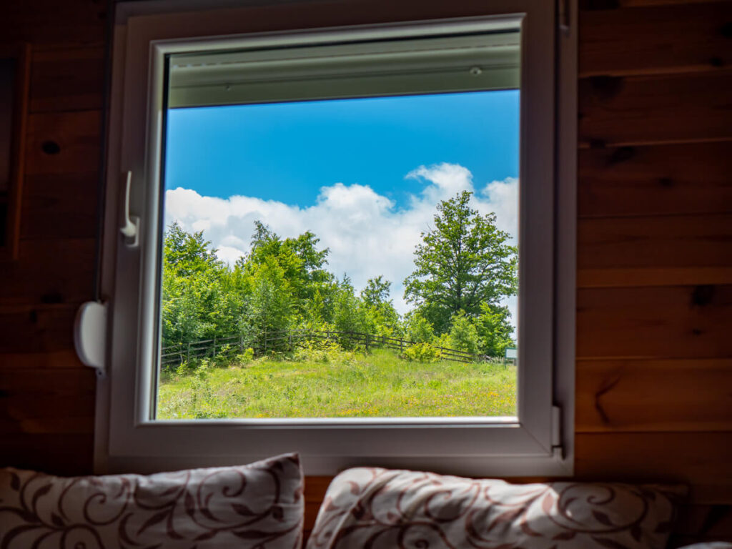 A cabin window revealing a view of forest and blue sky near Biogradska Gora.