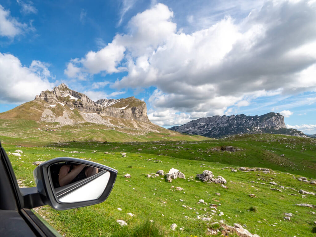A car wingmirror in front of a view of a green valley on the Durmitor Ring Road.