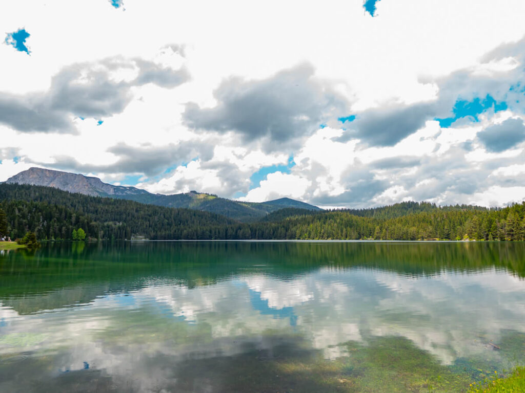 The dark Black Lake reflecting clouds in a sunny sky against its still surface.