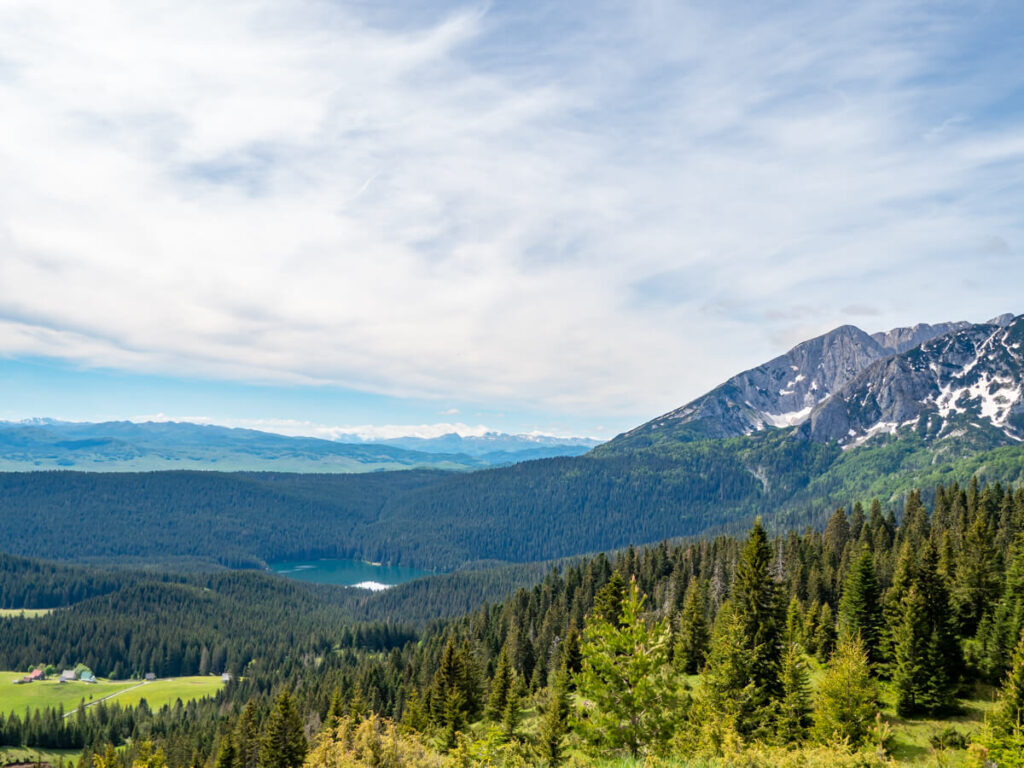 The Black Lake surrounded by forest beneath a snowy peak, viewed from a viewpoint on the Durmitor Ring Road.