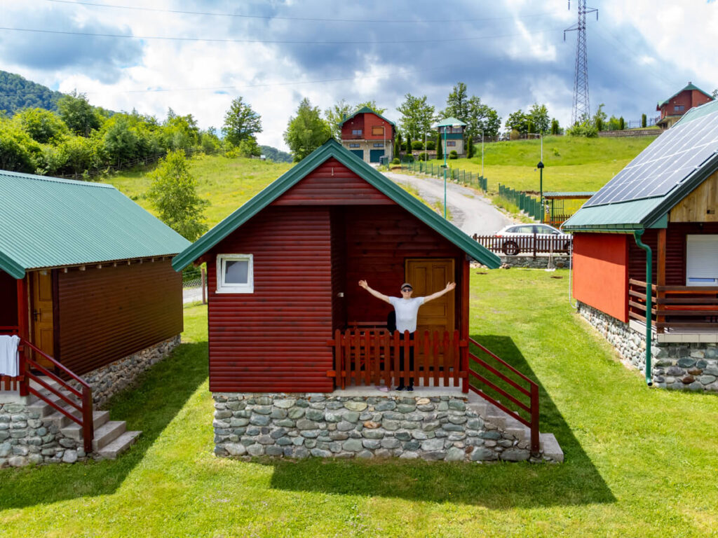 Dan standing on the porch of a wooden cabin at Eco Village Coric in Biogradska Gora with his arms out wide.