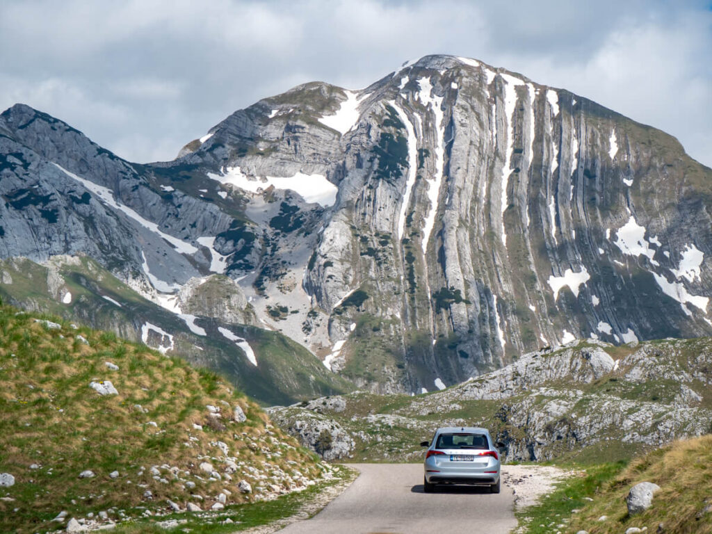 A silver car driving towards Mount Prutaš in Durmitor National Park.