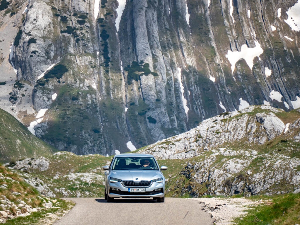 Dan driving a rental car in Durmitor National Park, with an impressive tall mountain looming in the background.