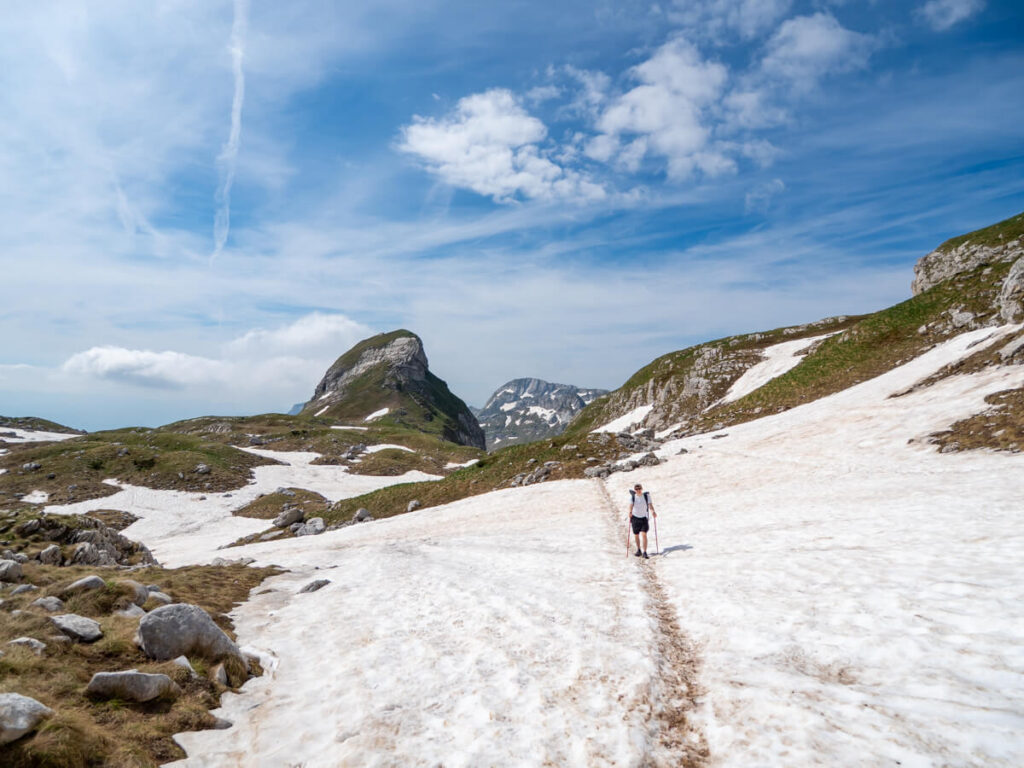 Dan hiking on a snowfield backed by green mountains and blue sky on the Bobotov Kuk trail.