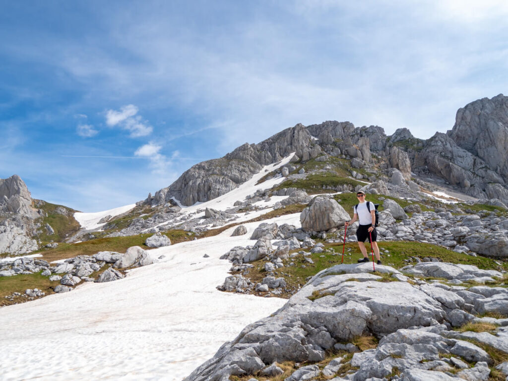 Dan hiking with trekking poles, standing on the side of a mountains covered in snow on the Bobotov Kuk trail.