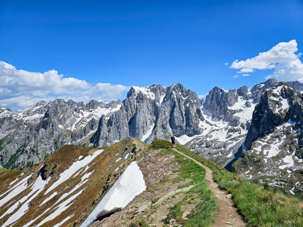 Dan in the distance on a narrow dirt path on the Three Peaks trail backed by the dramatic and snow-topped Karanfili mountains.