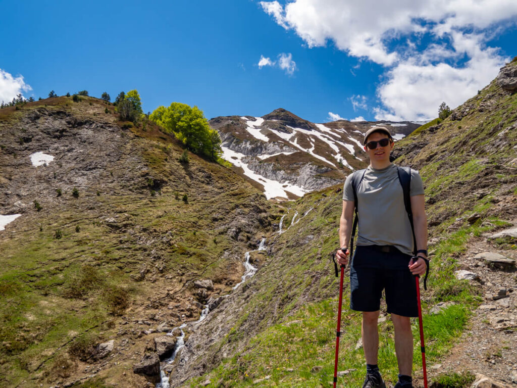 Dan standing beside a tall waterfall trickling into the meadow on the Three Peaks hike in Prokletije National Park.
