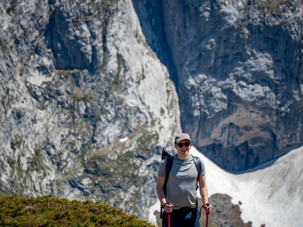 A close-up shot of Dan holding hiking poles and wearing a backpack in front of the impressive limestone cliffs of the Karanfili Massif, taken from the Three Peaks hike.