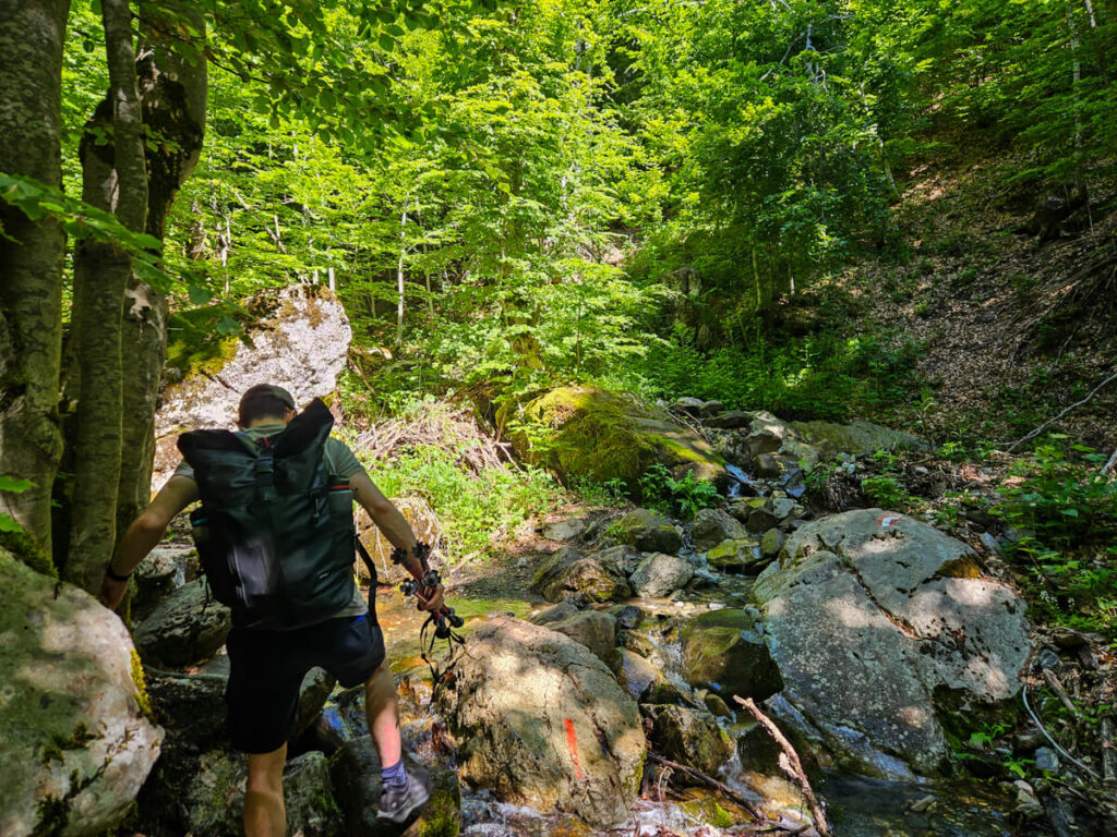 Dan crossing a rocky river in the forest on the Three Peaks trail in Prokletije National Park.