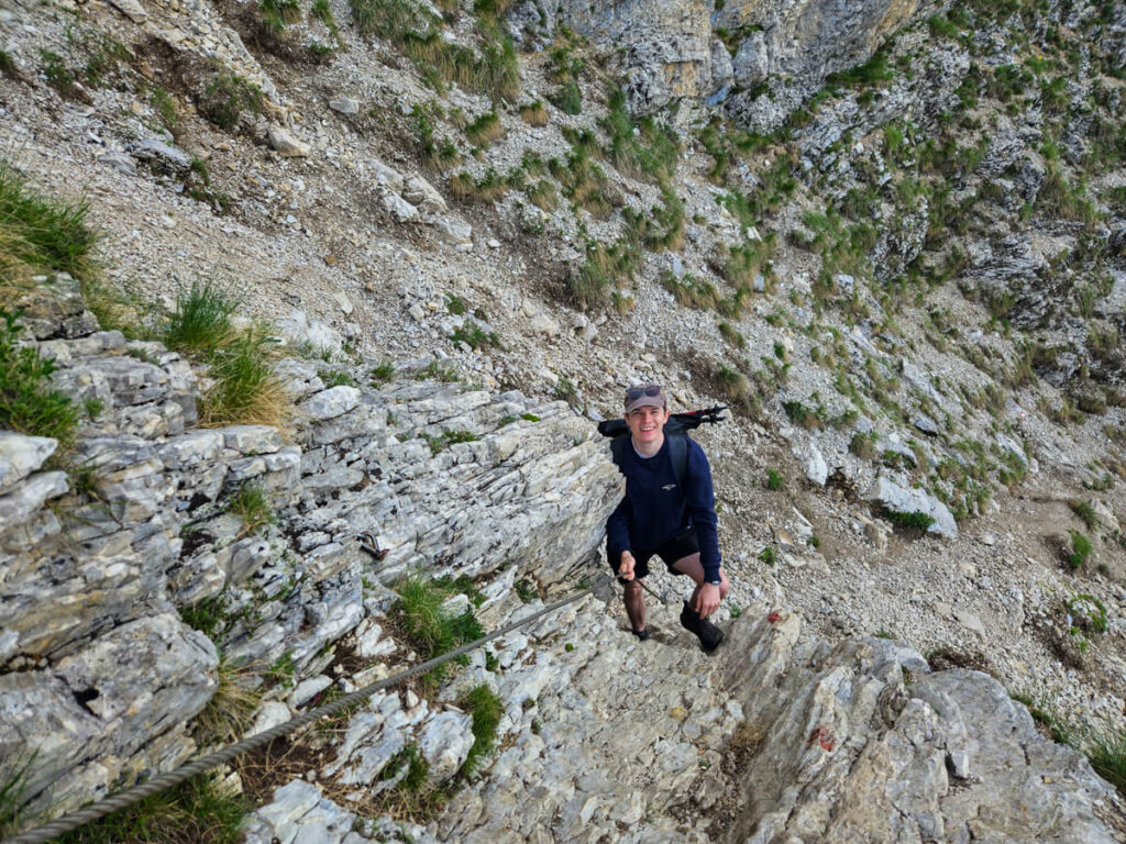 Dan climbing a narrow rockface while holding onto a steel cable on the Bobotov Kuk trail.