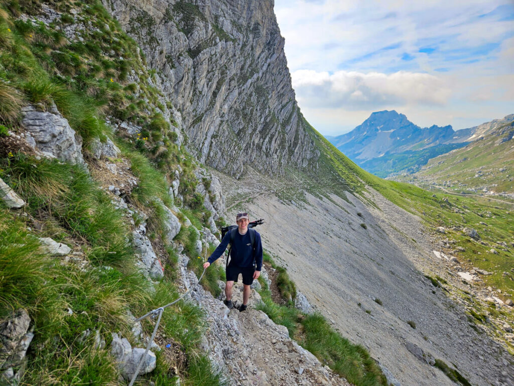 Dan holding a steel cable on a narrow scree trail approaching the scramble section of the Bobotov Kuk hike.