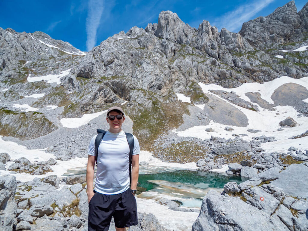 Dan standing in front of an icy blue glacial lake, Zeleni Vir, surrounded by snow, at the foot of Bobotov Kuk.