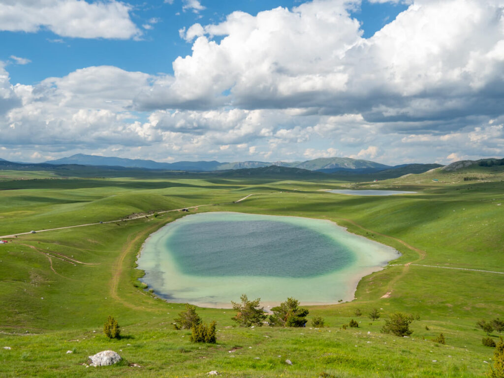 A two-tone blue lake with a dark centre and lighter shallow edge surrounded by green grass at Devil's Lake near Durmitor National Park.