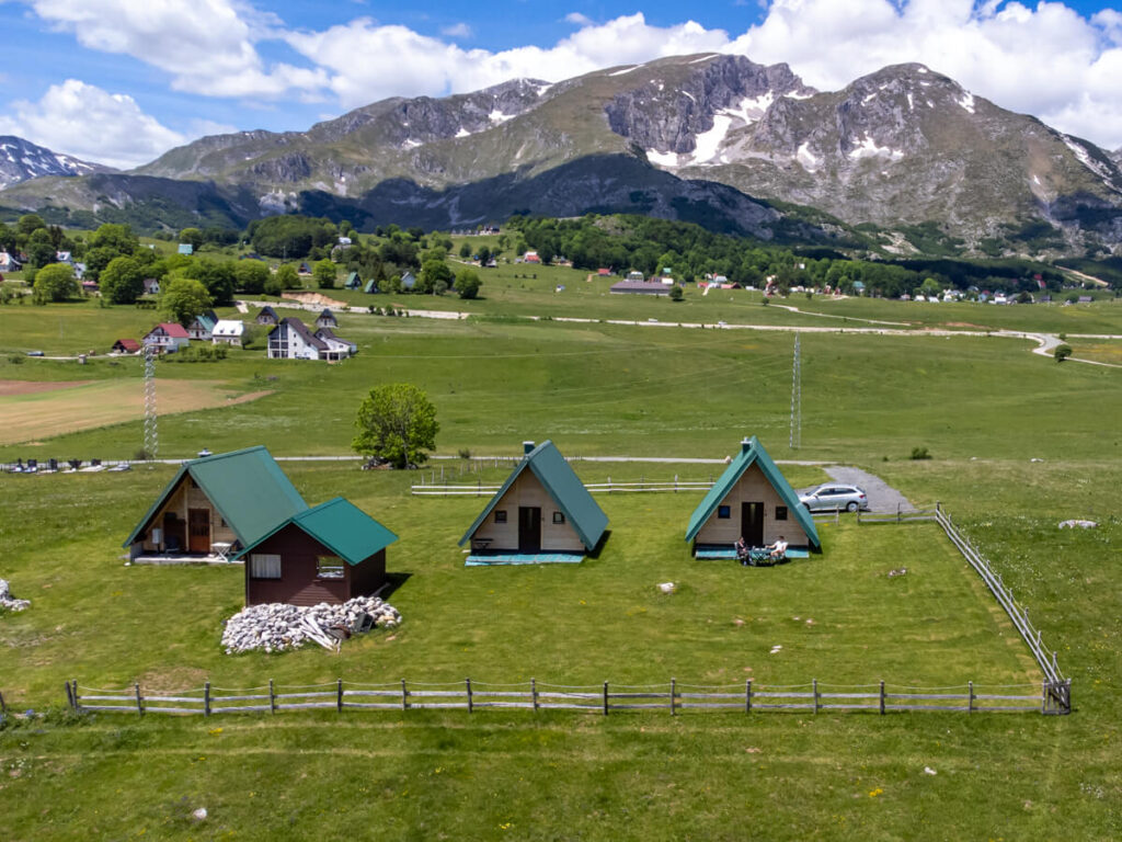Three A-frame wooden cabins sitting in the fields below Savin Kuk on the outskirts of Durmitor National Park.