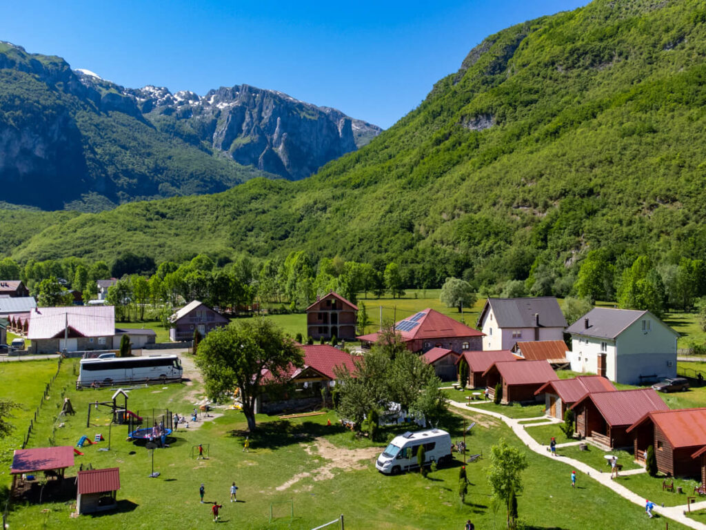 An aerial view of a campervan parked on the grass by a row of wooden cabins and a playground with lots of children at Eko Katun Rosi.