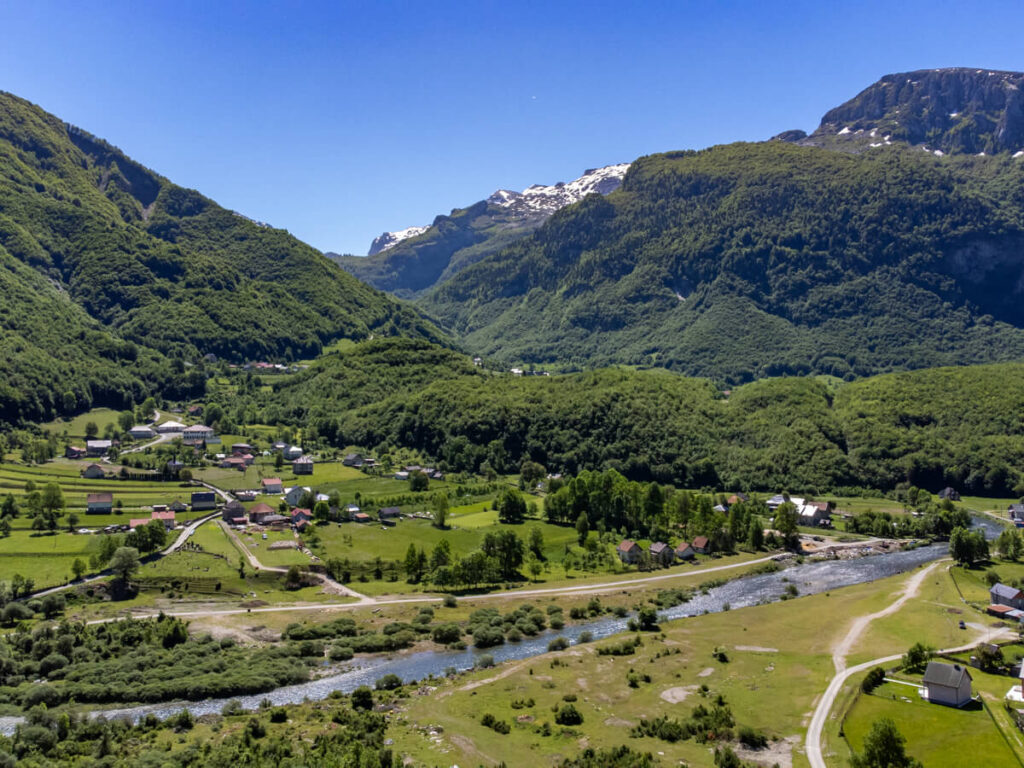 An aerial view of a river winding through the lush green Ropojana Valley in Prokletije National Park.