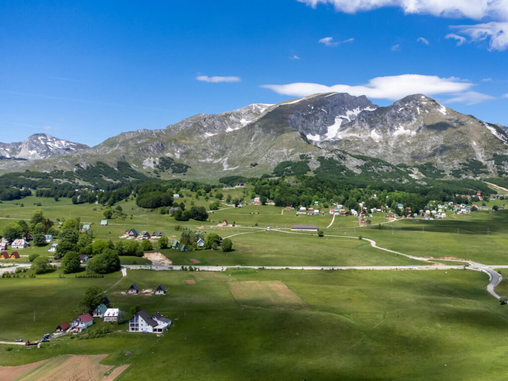 A drone shot of houses lying in a valley below a mountain range and Savin Kuk peak in Durmitor National Park.